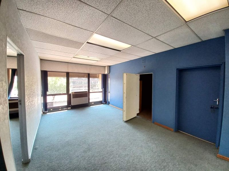 An empty office space featuring blue accent walls, a drop ceiling with recessed lighting, and large windows providing natural light.