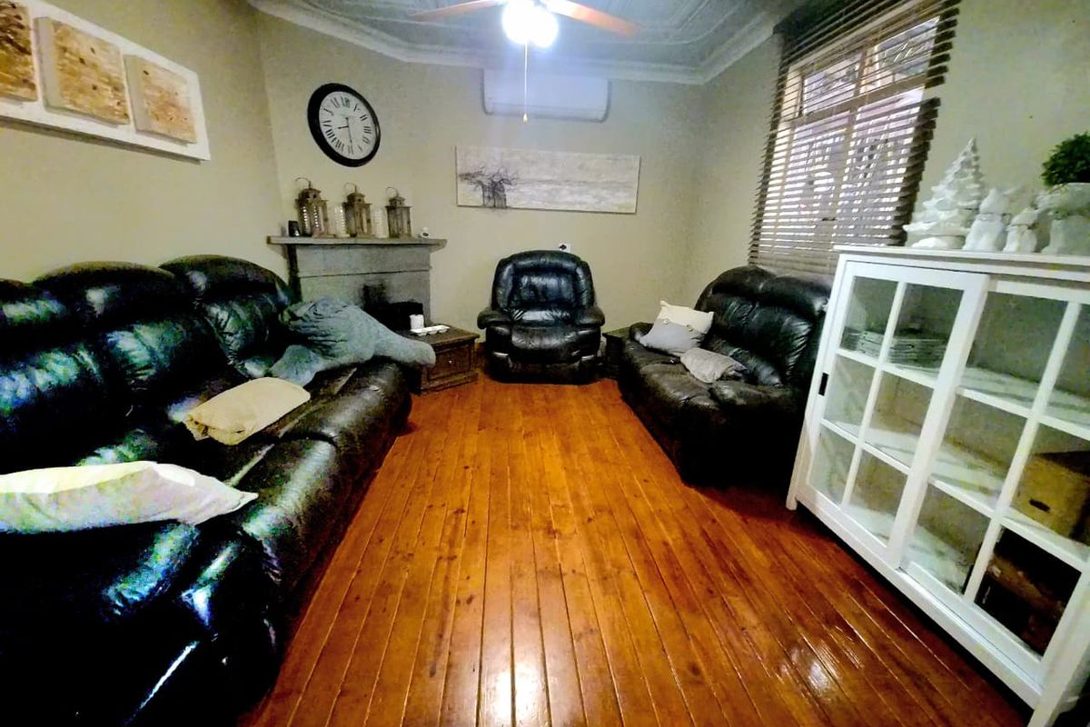 A living room featuring polished hardwood flooring, a decorative ceiling, a fireplace mantel, and a split system air conditioner.