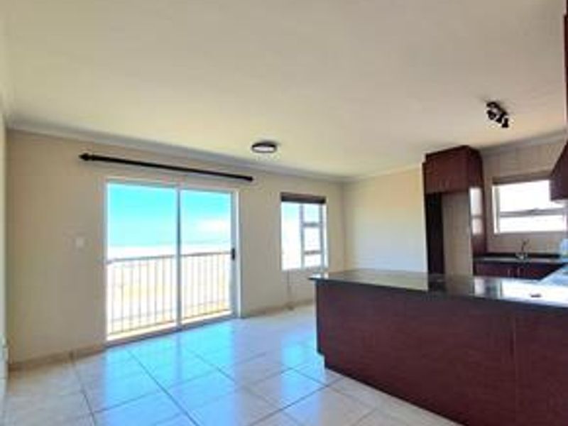 An open-plan living and kitchen area featuring tiled floors, a kitchen island with dark cabinetry, and a sliding door leading to a balcony.