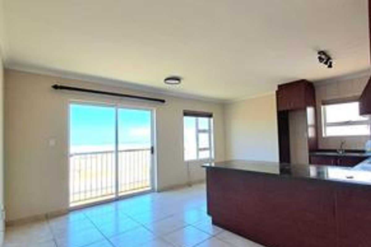 An open-plan living and kitchen area featuring tiled floors, a kitchen island with dark cabinetry, and a sliding door leading to a balcony.