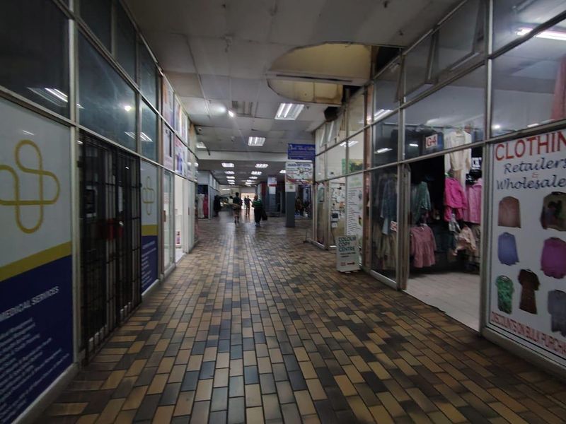 A commercial retail corridor featuring glass storefronts, tiled flooring, and a suspended ceiling with visible signs of wear and maintenance requirements.