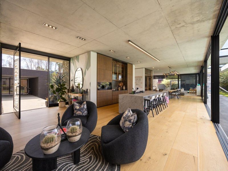 Spacious open-plan living and kitchen area featuring exposed concrete ceilings, timber flooring, and seamless indoor-outdoor flow through large sliding glass doors.