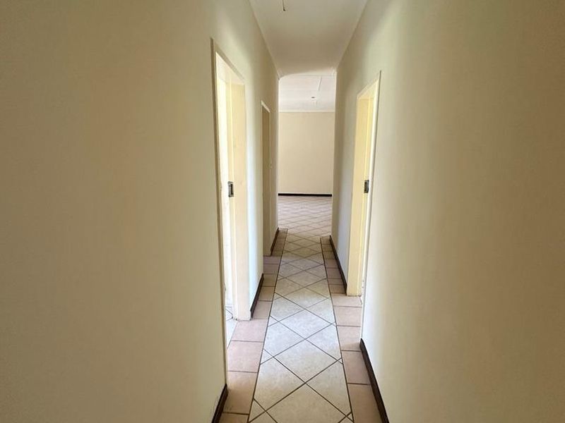 A clean, empty hallway featuring neutral wall paint and diagonal ceramic floor tiling, providing access to adjacent rooms.