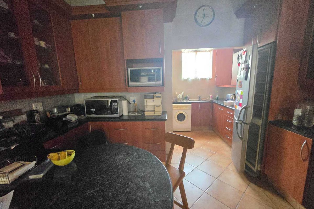 A functional kitchen featuring dark wood cabinetry, granite countertops, and an adjoining scullery area with tiled flooring and built-in storage.