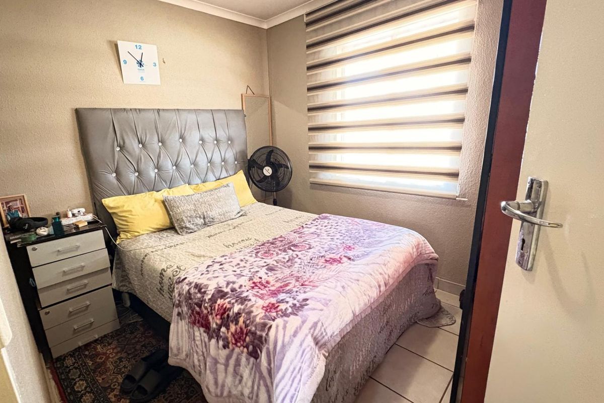 A compact bedroom featuring tiled flooring, a window with fitted zebra blinds, and a standard door.