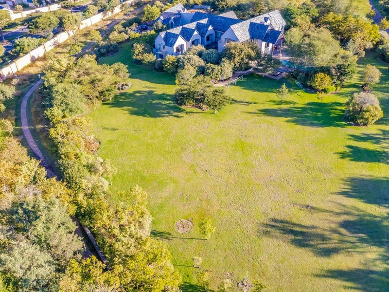 Aerial view of a large residential property featuring expansive green lawns, mature trees, and a paved walking path.