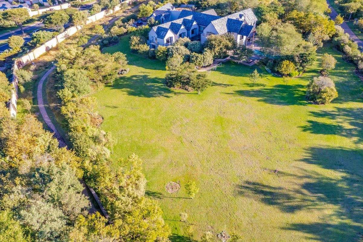 Aerial view of a large residential property featuring expansive green lawns, mature trees, and a paved walking path.