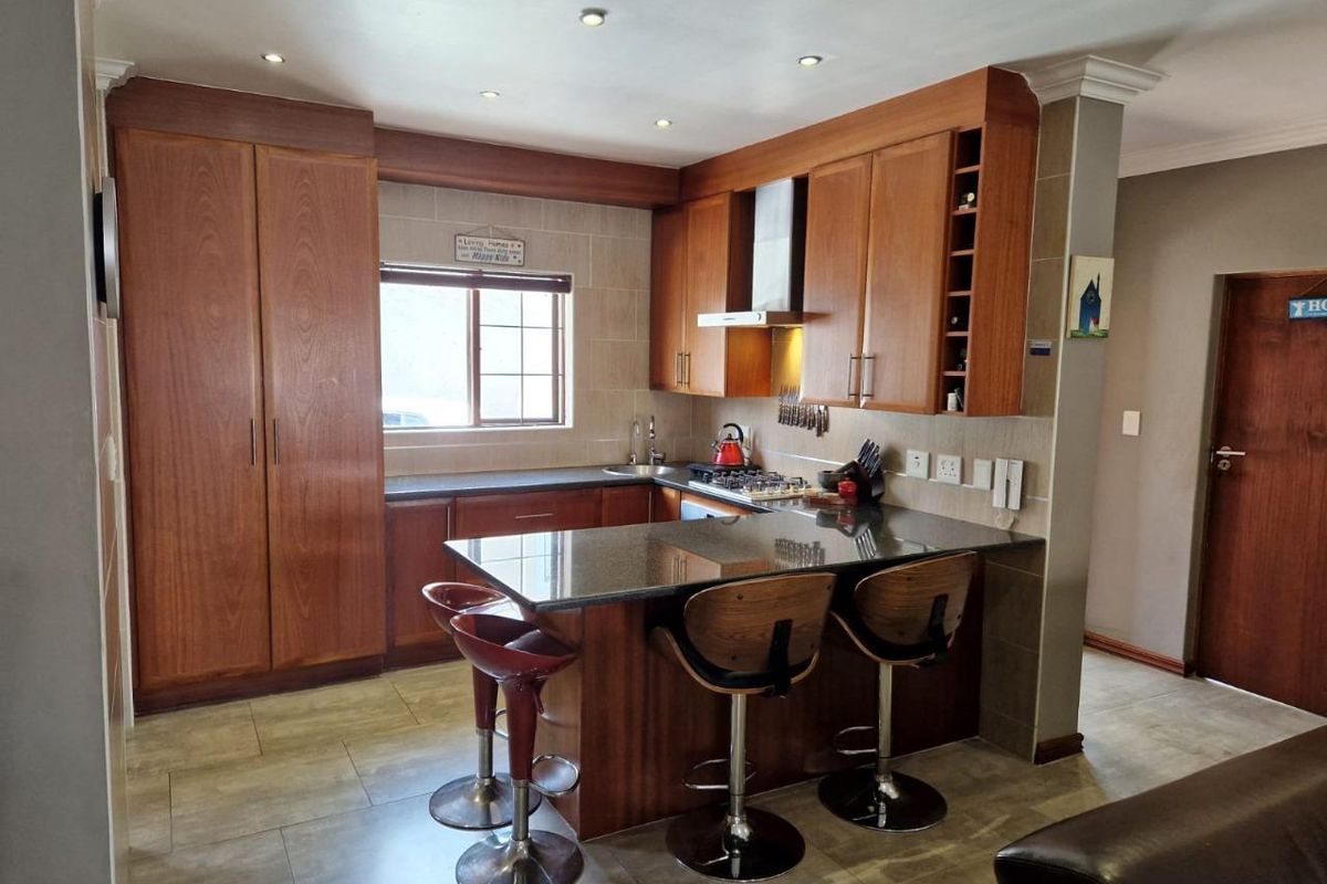 A well-maintained kitchen featuring wooden cabinetry, granite countertops, a breakfast bar, and integrated stainless steel appliances including a hob and extractor fan.