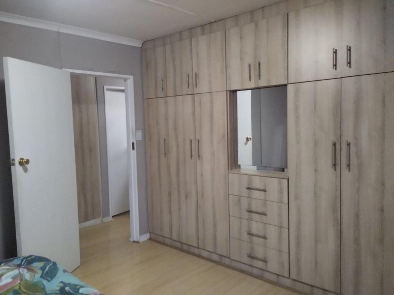 Bedroom featuring extensive light wood-grain built-in cupboards with integrated drawers and mirror, complemented by laminate flooring and neutral wall finishes.