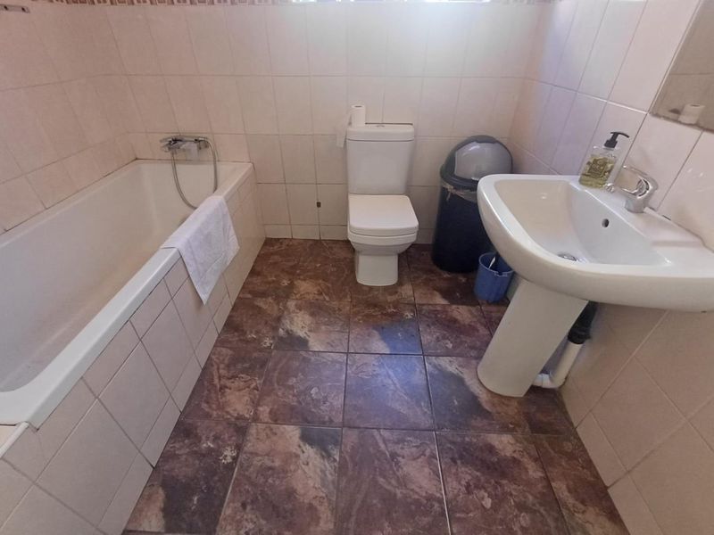 A functional bathroom featuring a bathtub, pedestal basin, and toilet with tiled walls and flooring, currently showing signs of wear.