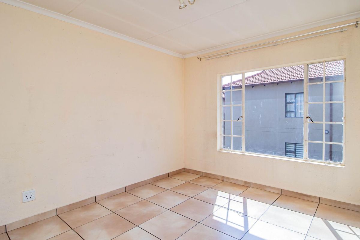 An empty bedroom featuring tiled flooring, a large window with metal frames, and neutral wall finishes.