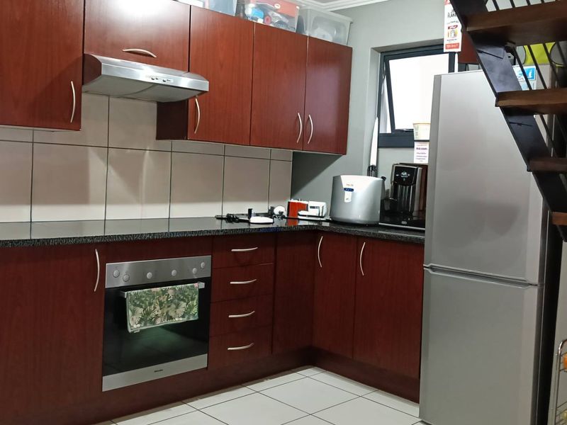 A functional kitchen featuring dark wood cabinetry, granite countertops, built-in oven, extractor fan, and tiled flooring, conveniently located adjacent to the staircase.