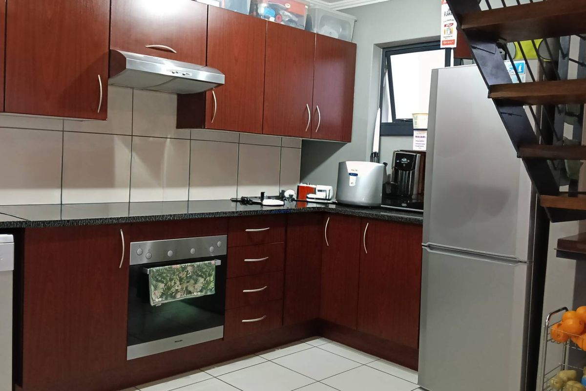 A functional kitchen featuring dark wood cabinetry, granite countertops, built-in oven, extractor fan, and tiled flooring, conveniently located adjacent to the staircase.