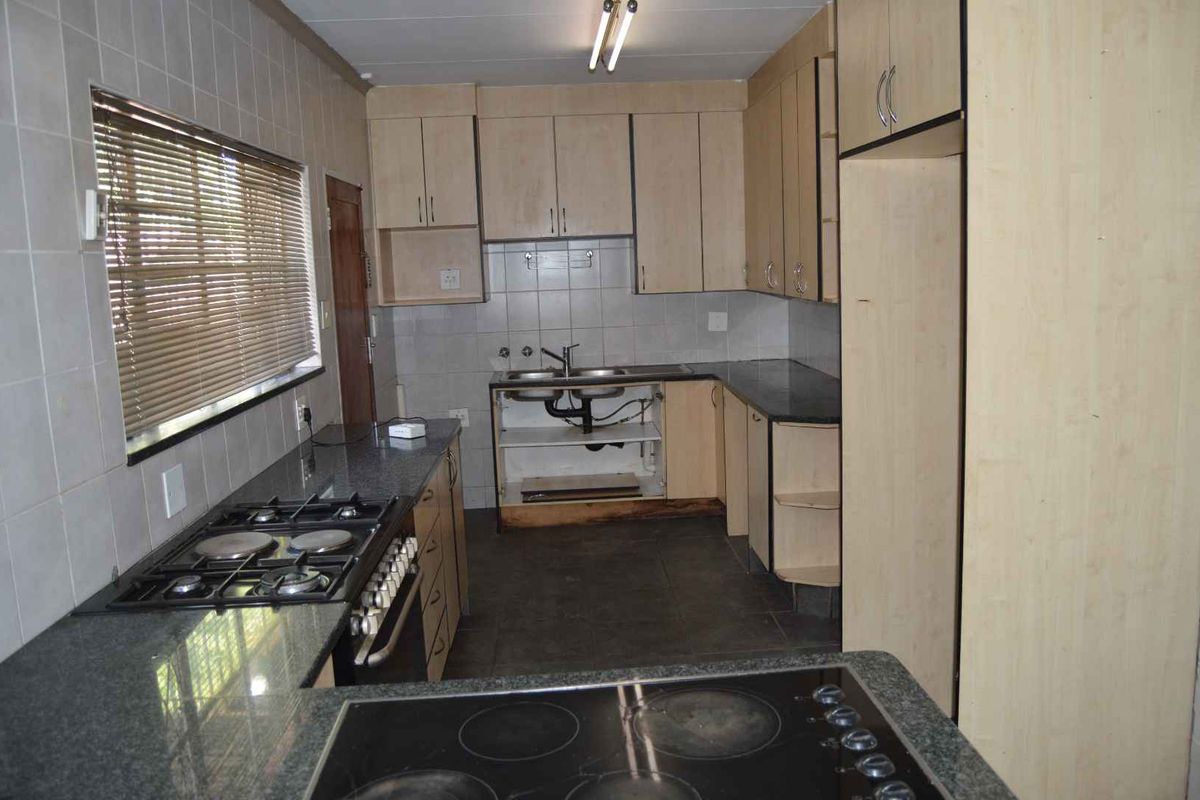 A functional kitchen featuring granite countertops, dual hobs, and tiled finishes, currently requiring repairs to the cabinetry under the sink area.