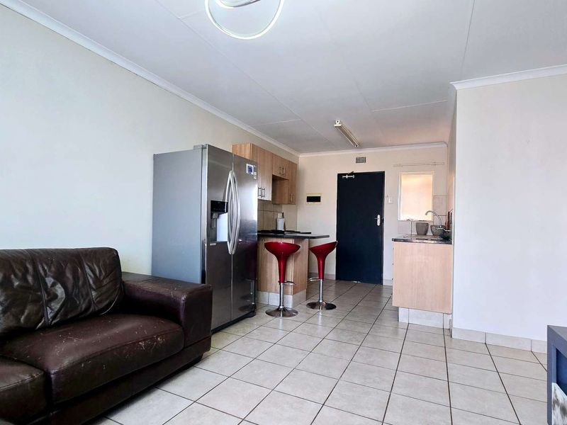 Open plan living area featuring tiled flooring and a compact kitchen with built-in cabinetry and a breakfast bar.