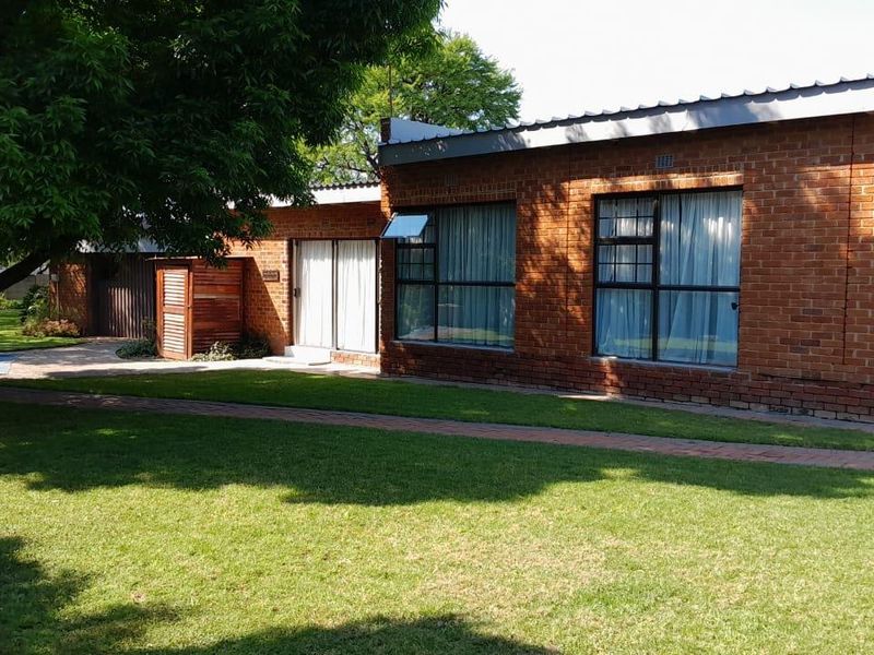 Rear view of a brick house featuring large windows, a sliding glass door, and a well-maintained garden with a paved walkway.