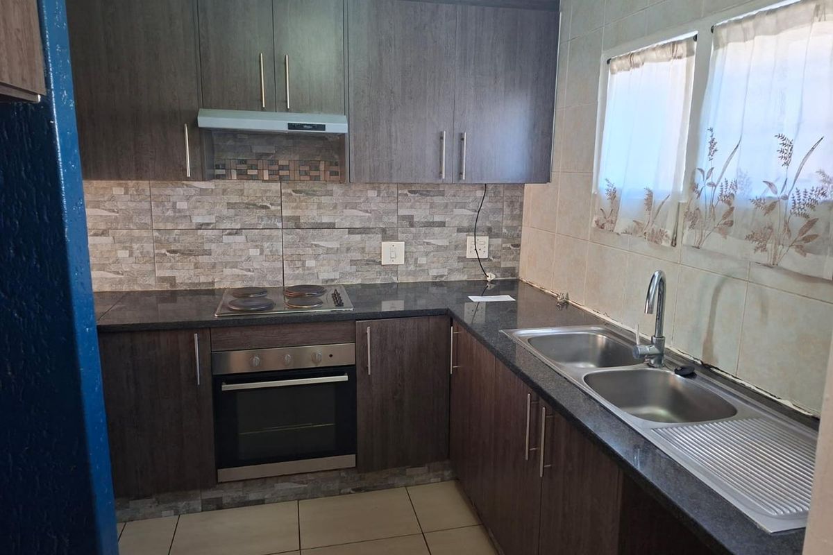Functional kitchen featuring dark wood cabinetry, granite countertops, a built-in oven, electric hob, extractor fan, and a double stainless steel sink.