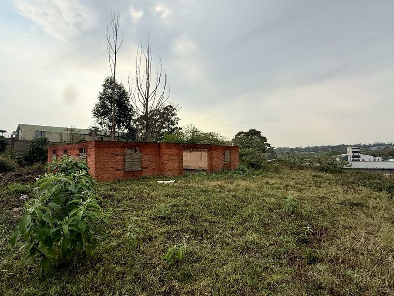 A view of a derelict brick structure on a vacant commercial plot, featuring boarded windows and significant structural deterioration.