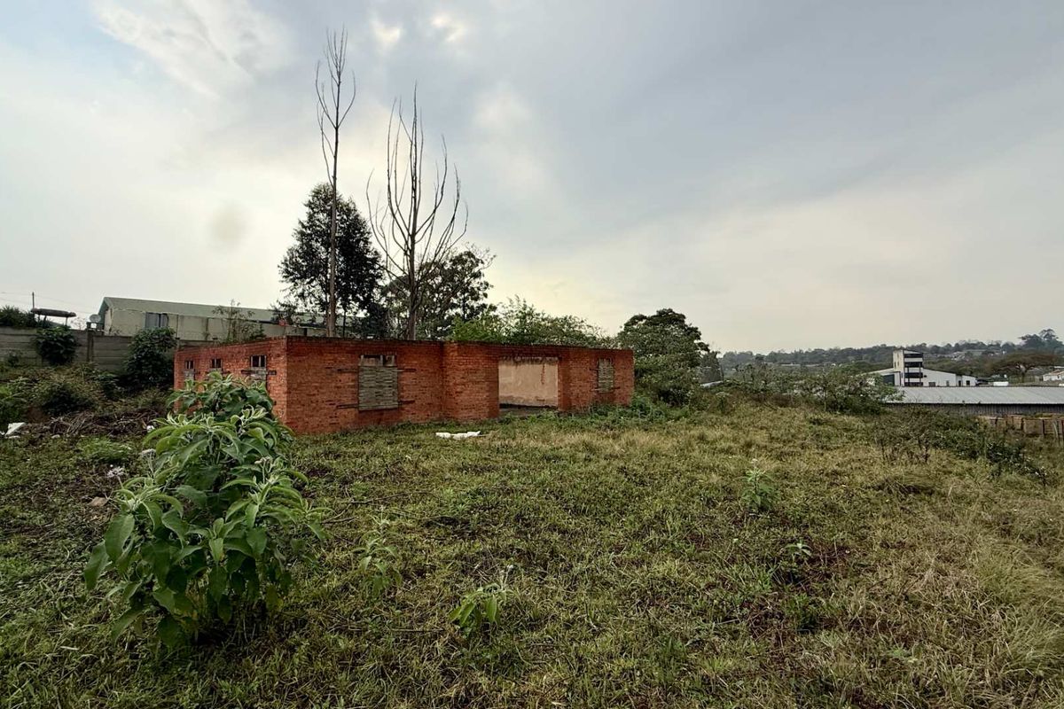 A view of a derelict brick structure on a vacant commercial plot, featuring boarded windows and significant structural deterioration.