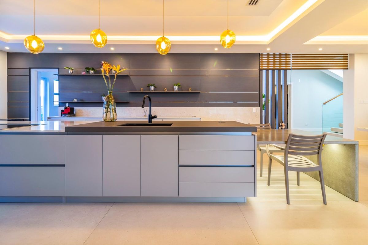 A modern, high-end kitchen featuring a central island with a sleek sink, minimalist cabinetry, and elegant pendant lighting in a bright, open-plan space.