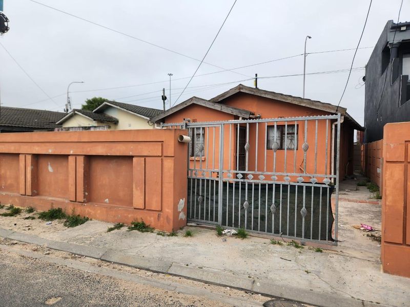 Front view of a single-story house featuring a perimeter wall, metal security gate, and tiled roof, showing signs of exterior wear.
