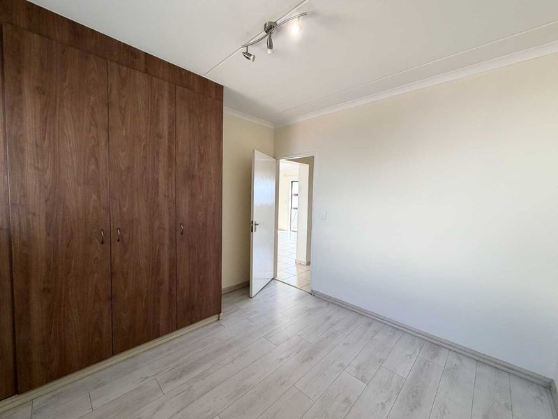 A bright, empty bedroom featuring modern wood-look laminate flooring and extensive built-in wooden cupboards, offering a clean and neutral space.
