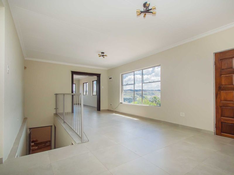 Spacious upper-level landing or hallway featuring neutral tiled flooring, a metal balustrade, and a large window offering scenic views.