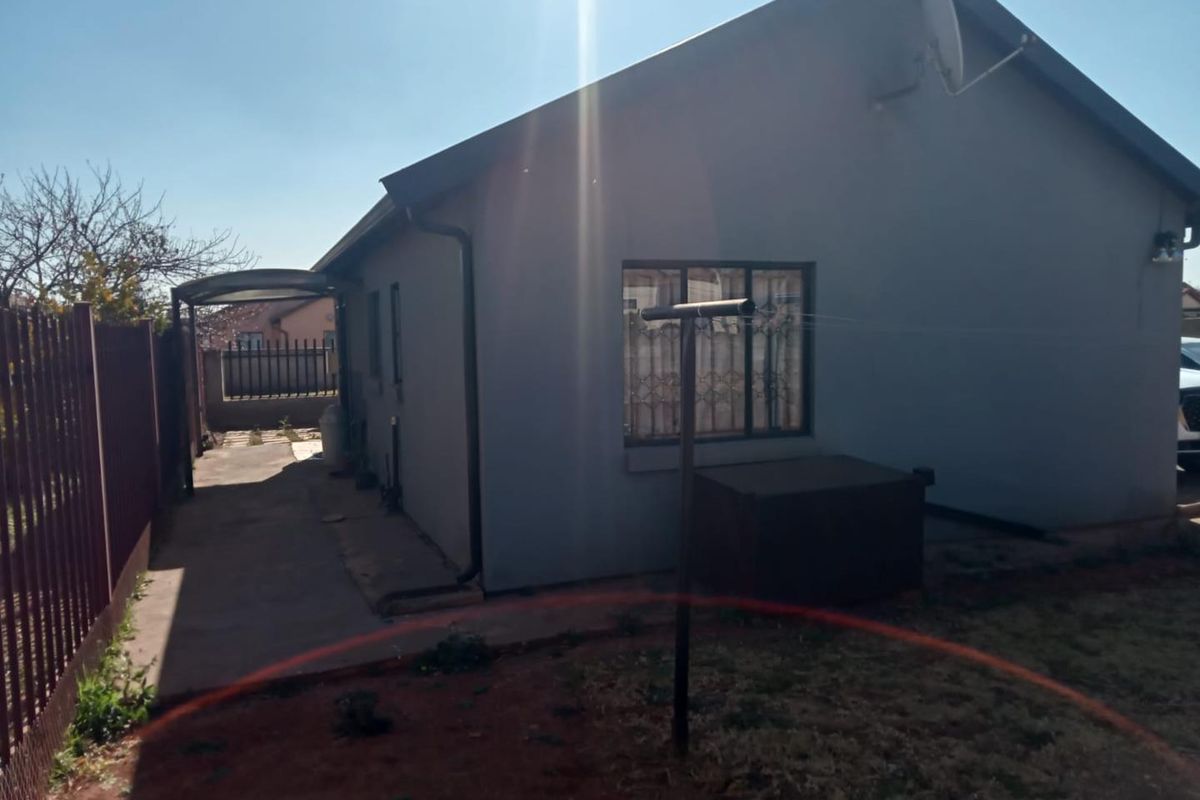 Rear view of the property showing a concrete pathway, perimeter fencing, and exterior wall with a satellite dish installation.