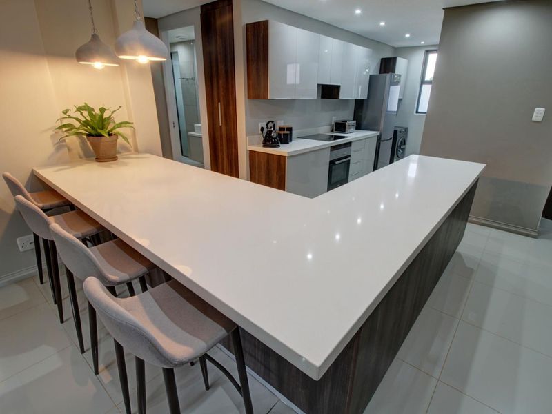 Modern open-plan kitchen featuring a large quartz breakfast bar, sleek built-in cabinetry, integrated appliances, and recessed lighting, creating a functional and contemporary living space.