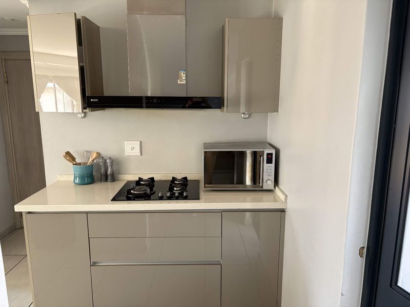 A compact, modern kitchen featuring high-gloss cabinetry, a stone countertop, a built-in gas hob, an extractor fan, and a microwave.