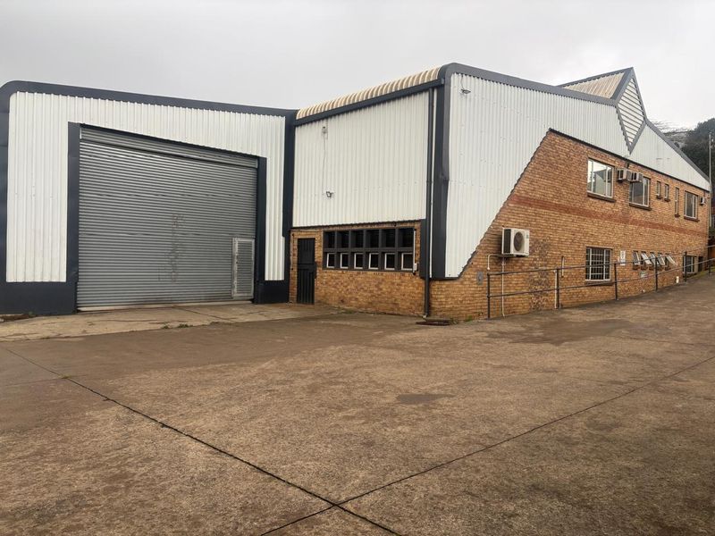 Industrial warehouse facility featuring a large roller shutter door, face brick and corrugated metal exterior, and a spacious concrete yard area.