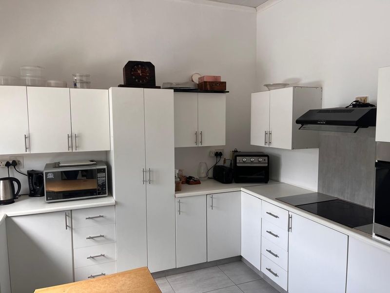 A functional kitchen featuring white cabinetry, laminate countertops, an electric hob with extractor fan, and tiled flooring.
