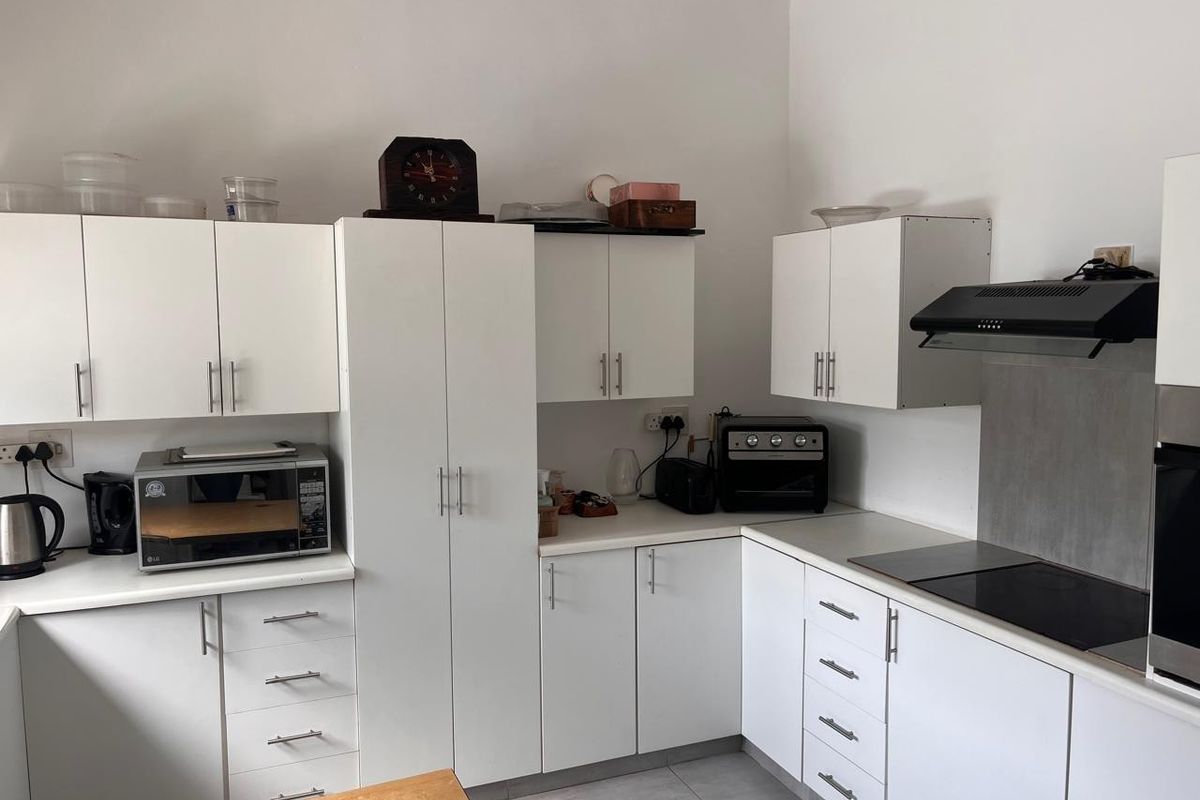 A functional kitchen featuring white cabinetry, laminate countertops, an electric hob with extractor fan, and tiled flooring.