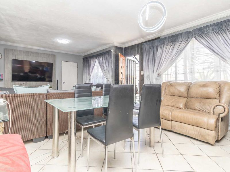 Open-plan living and dining area featuring tiled flooring, a decorative feature wall, and modern lighting fixtures.
