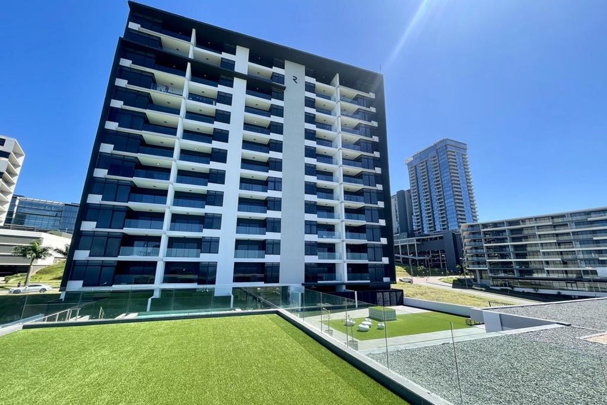 A modern high-rise apartment building featuring glass balconies, a landscaped rooftop terrace with artificial turf, and contemporary architectural design.