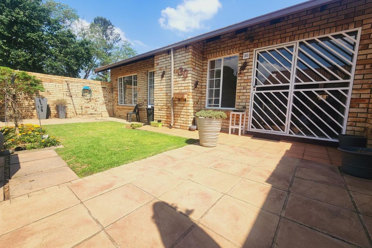 A private rear garden featuring a paved patio area, face brick exterior, and a well-maintained lawn enclosed by a boundary wall.