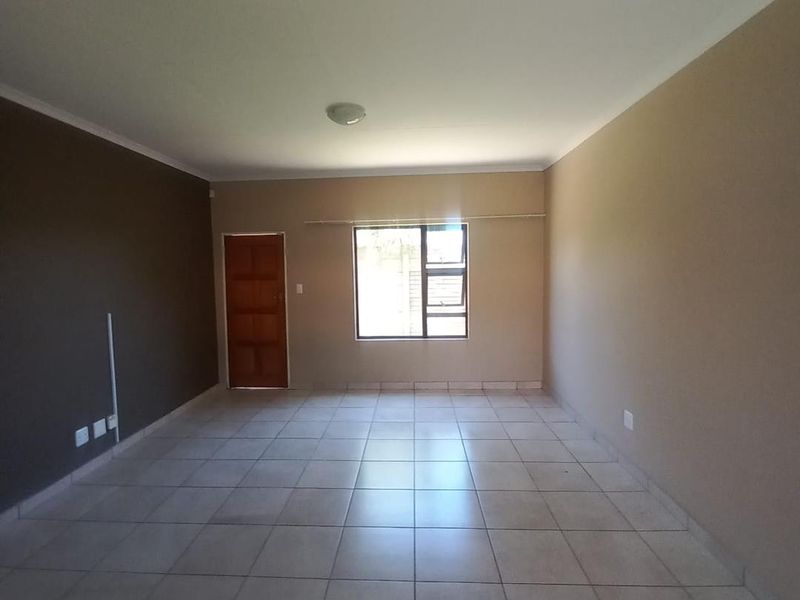 A spacious, empty living area featuring neutral wall tones, tiled flooring, and natural light through a central window.