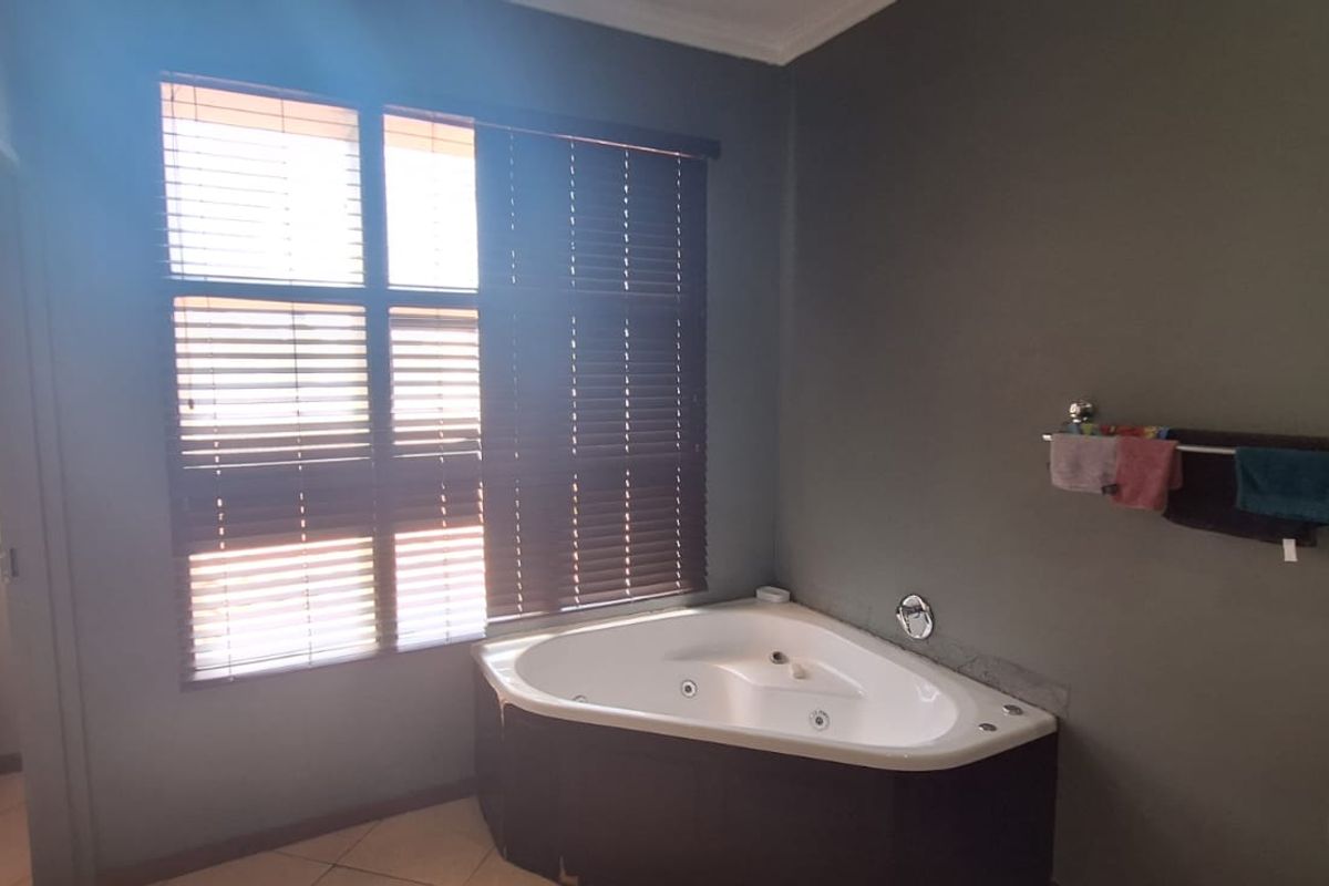 A bathroom featuring a corner jetted bathtub, tiled flooring, and dark grey walls, complemented by a large window with fitted wooden blinds.