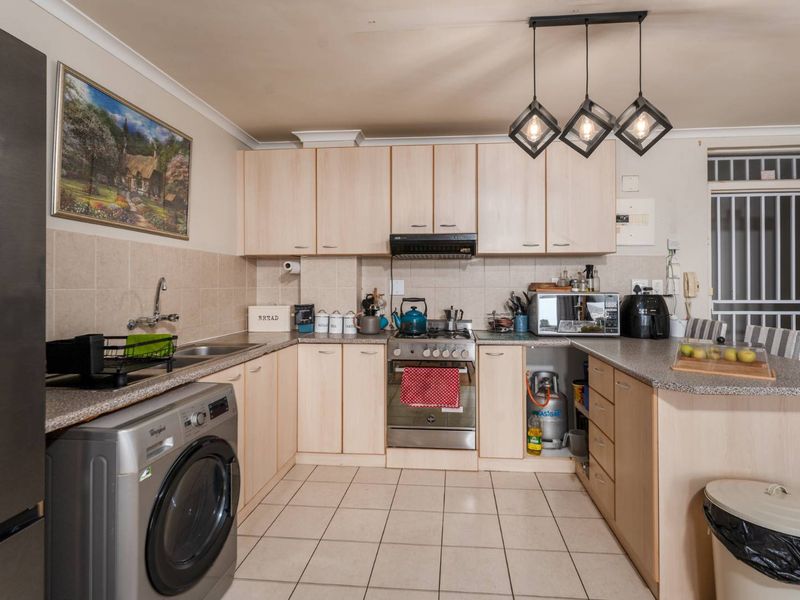 Functional kitchen featuring light wood-finish cabinetry, granite-look countertops, tiled flooring, gas stove with extractor, and a dedicated space for a washing machine.