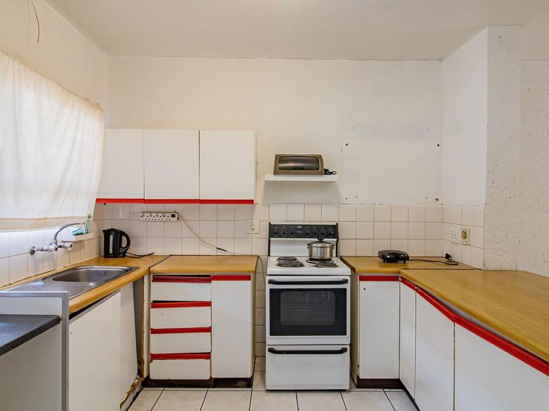 A dated kitchen featuring original white cabinetry with red trim, laminate countertops, a tiled backsplash, and a freestanding stove, offering significant renovation potential.
