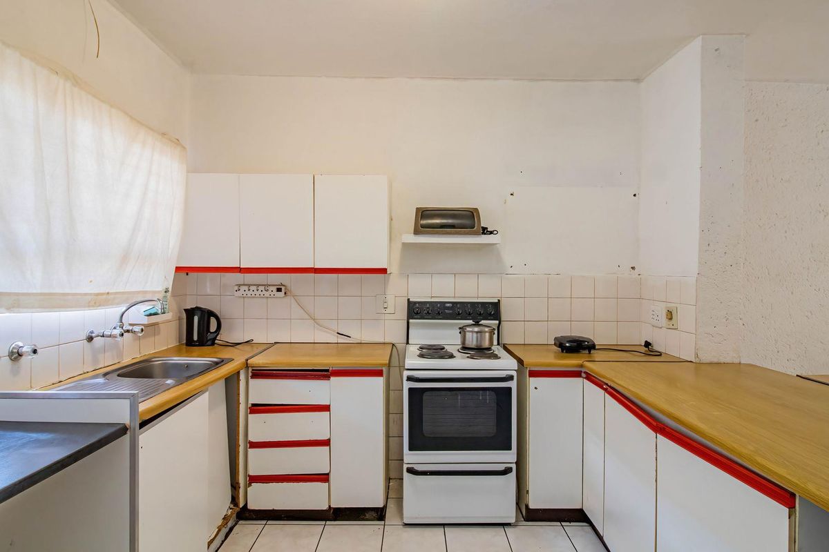 A dated kitchen featuring original white cabinetry with red trim, laminate countertops, a tiled backsplash, and a freestanding stove, offering significant renovation potential.