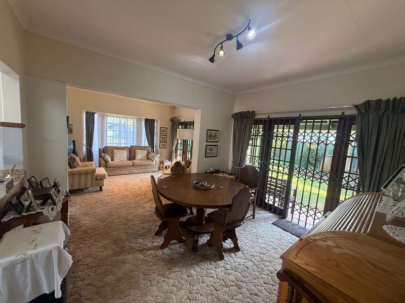 Spacious open-plan living and dining area featuring large windows, sliding security doors leading to the garden, and neutral wall finishes.
