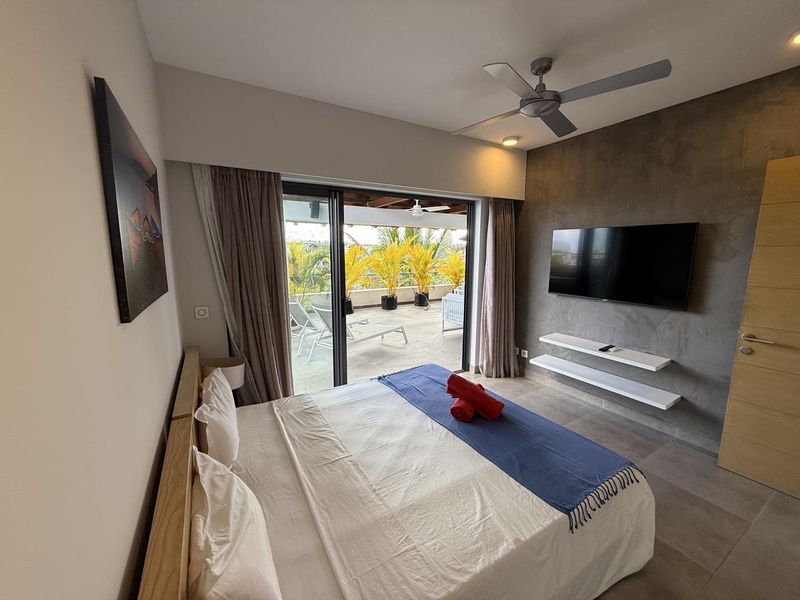 Modern bedroom featuring a concrete accent wall, ceiling fan, and large sliding glass doors opening onto a private balcony.