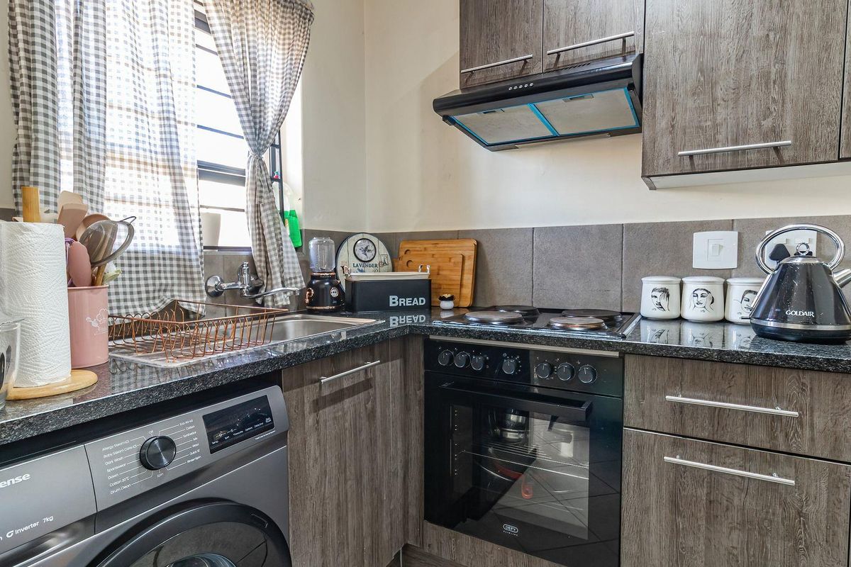 Compact kitchen featuring modern wood-grain cabinetry, granite countertops, a built-in oven with hob, extractor fan, and integrated laundry plumbing.