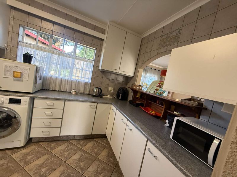 A functional kitchen featuring white cabinetry, laminate countertops, tiled backsplash, and a convenient archway opening into the adjacent living space.