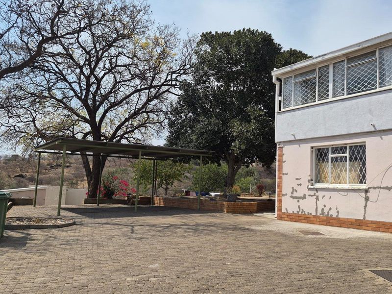 Rear exterior view featuring a paved driveway, carport, and a two-story building structure with visible wear to the exterior wall finishes.