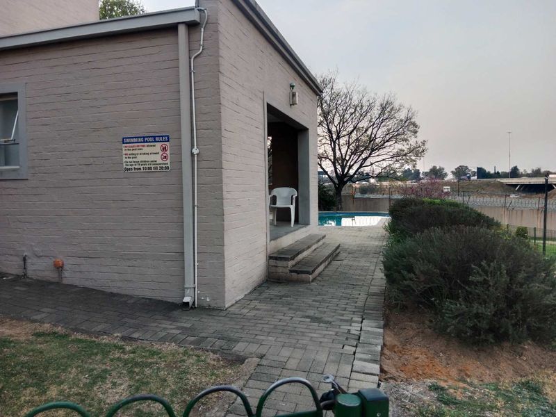 Exterior view of a communal swimming pool area featuring paved walkways and brick building structure.