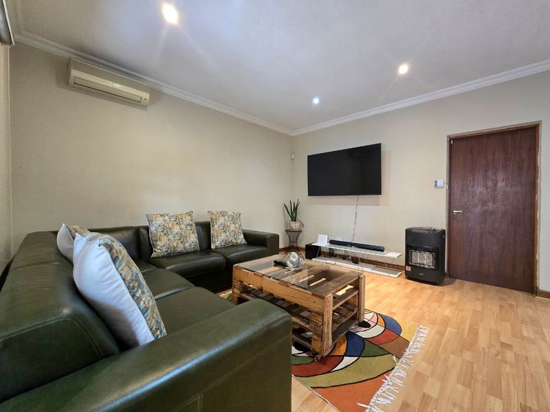 A comfortable living room featuring laminate flooring, recessed downlighting, and a wall-mounted air conditioning unit.