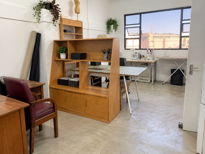 A functional industrial office space featuring polished concrete flooring, ample natural light from a large window, and efficient overhead fluorescent lighting.