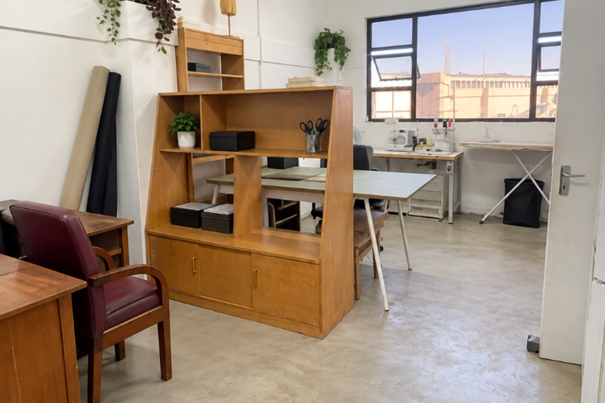 A functional industrial office space featuring polished concrete flooring, ample natural light from a large window, and efficient overhead fluorescent lighting.